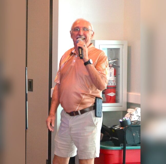 Man in an orange polo singing into a microphone at karaoke night
